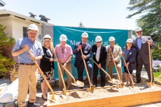 group of people wearing hard hats pose with shovels for ceremonial ground breaking