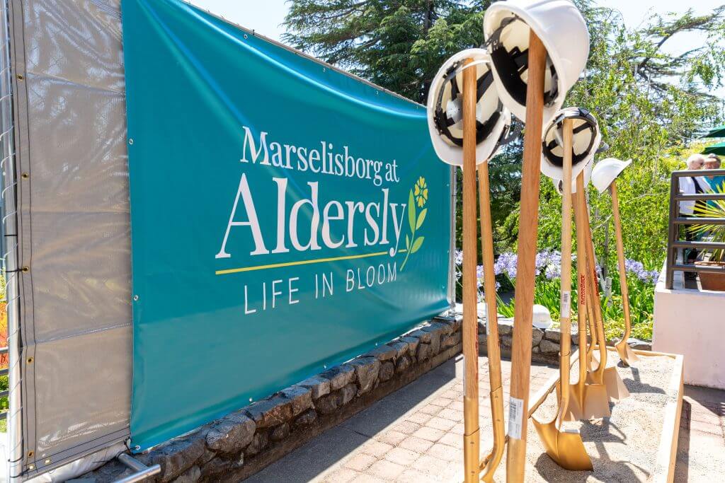image from groundbreaking ceremony for Aldersly featuring ceremonial shovels and hardhats with community banner in the background