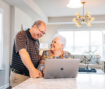 older couple smiling at each other at their kitchen island with a laptop