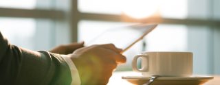 man holding tablet with cup of coffee on table